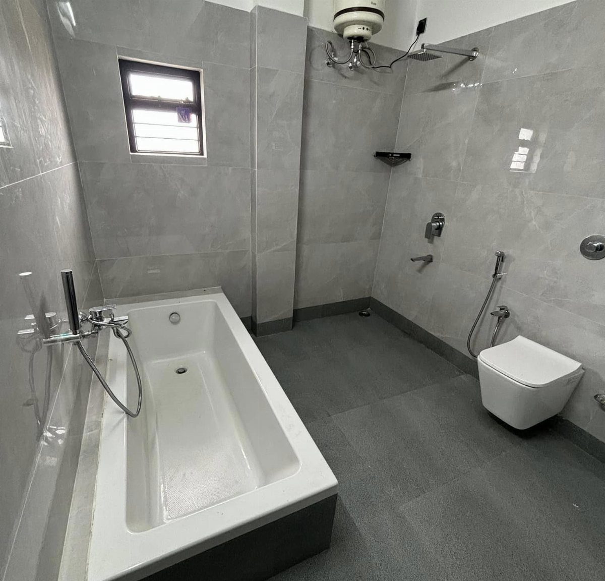 Modern grey tiled bathroom featuring a white rectangular bathtub and wall-mounted toilet.