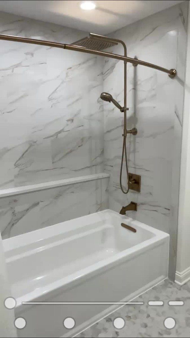 White bathtub and shower combo with gold fixtures and white marble walls.