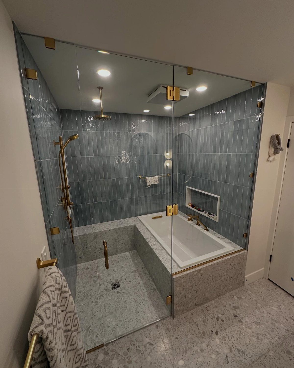 Modern bathroom wet room with blue tiles, white bathtub, and gold shower fixtures.