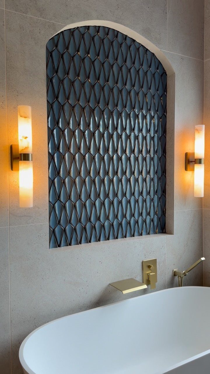 White freestanding bathtub with gold fixtures and a blue patterned tile wall niche.