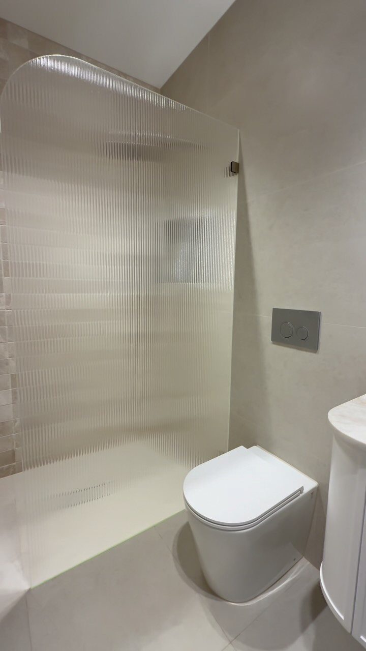 Modern bathroom with ribbed glass shower partition, white toilet, and neutral beige walls.