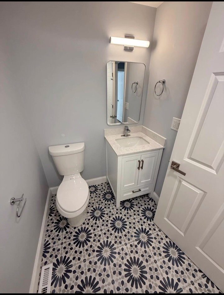 Small bathroom with grey walls, white vanity, and blue patterned floral floor tiles.