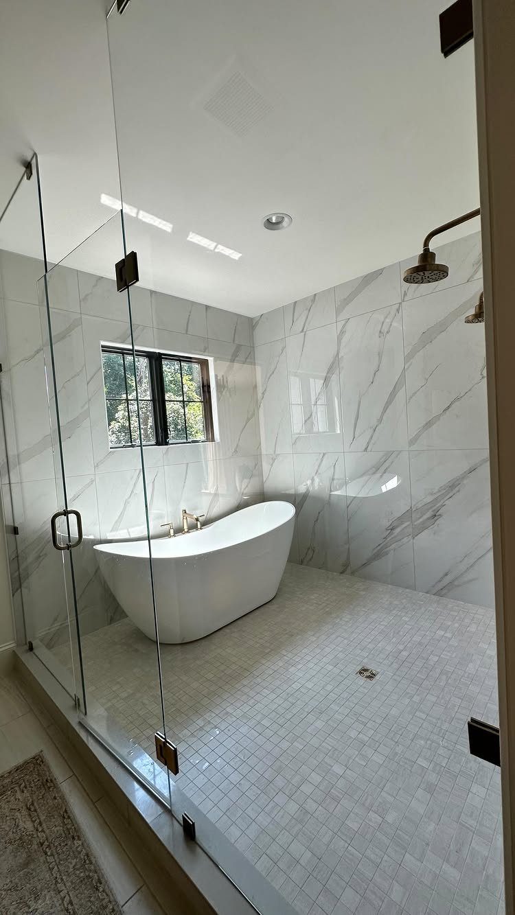 Curbless shower with white marble walls, glass panels, and a freestanding white bathtub.