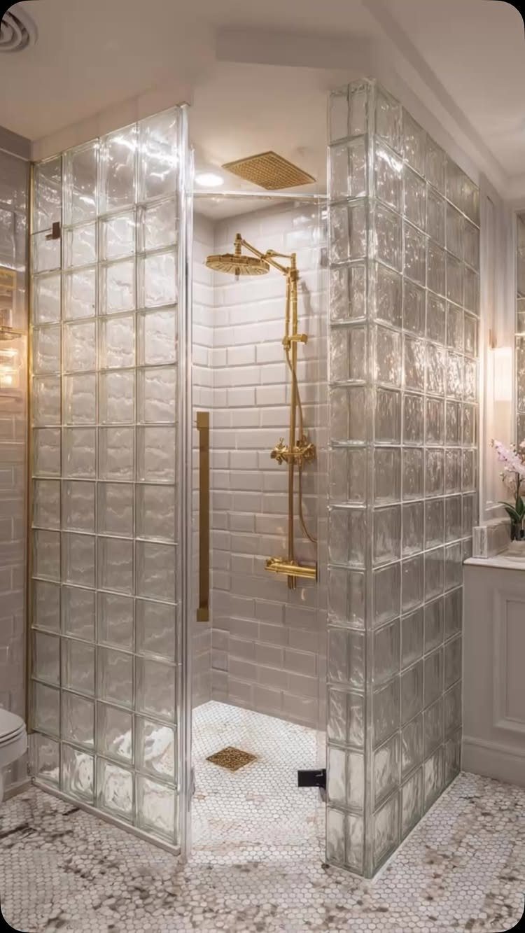 Modern shower with glass block walls, gold fixtures, and white pebble flooring.