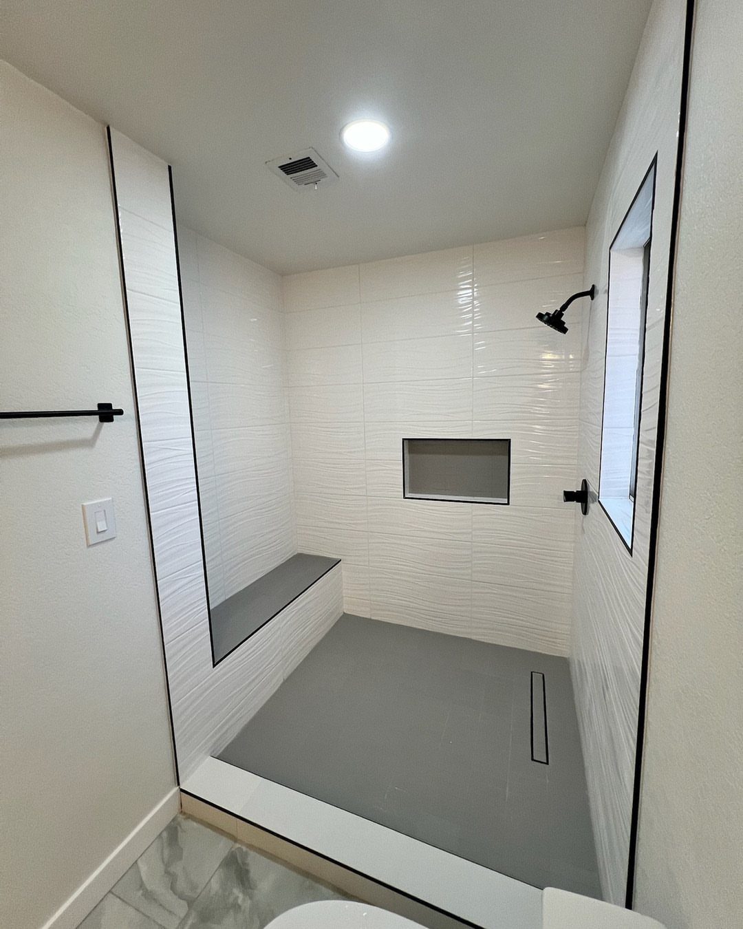 Modern walk-in shower with white tiles, grey flooring, and a built-in stone bench.