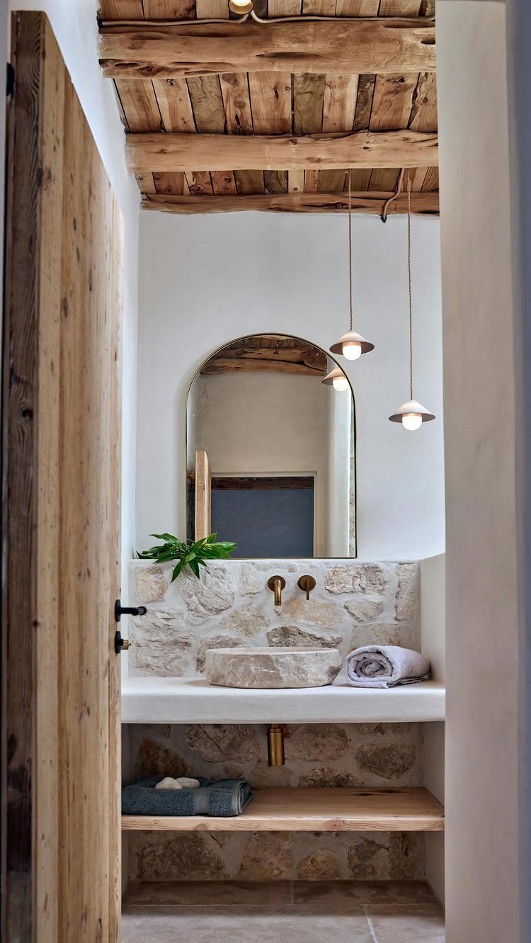 Rustic bathroom with wooden ceiling, stone vessel sink, and stone tiled walls.