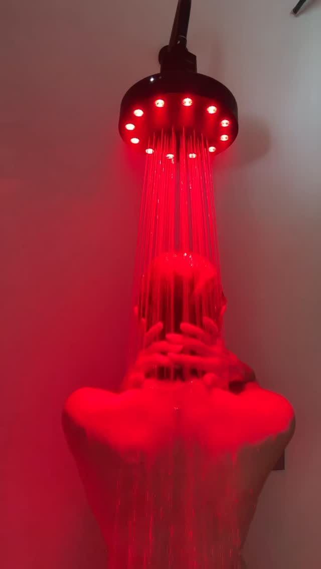 Red-lit shower head spraying water over a person's head and shoulders.