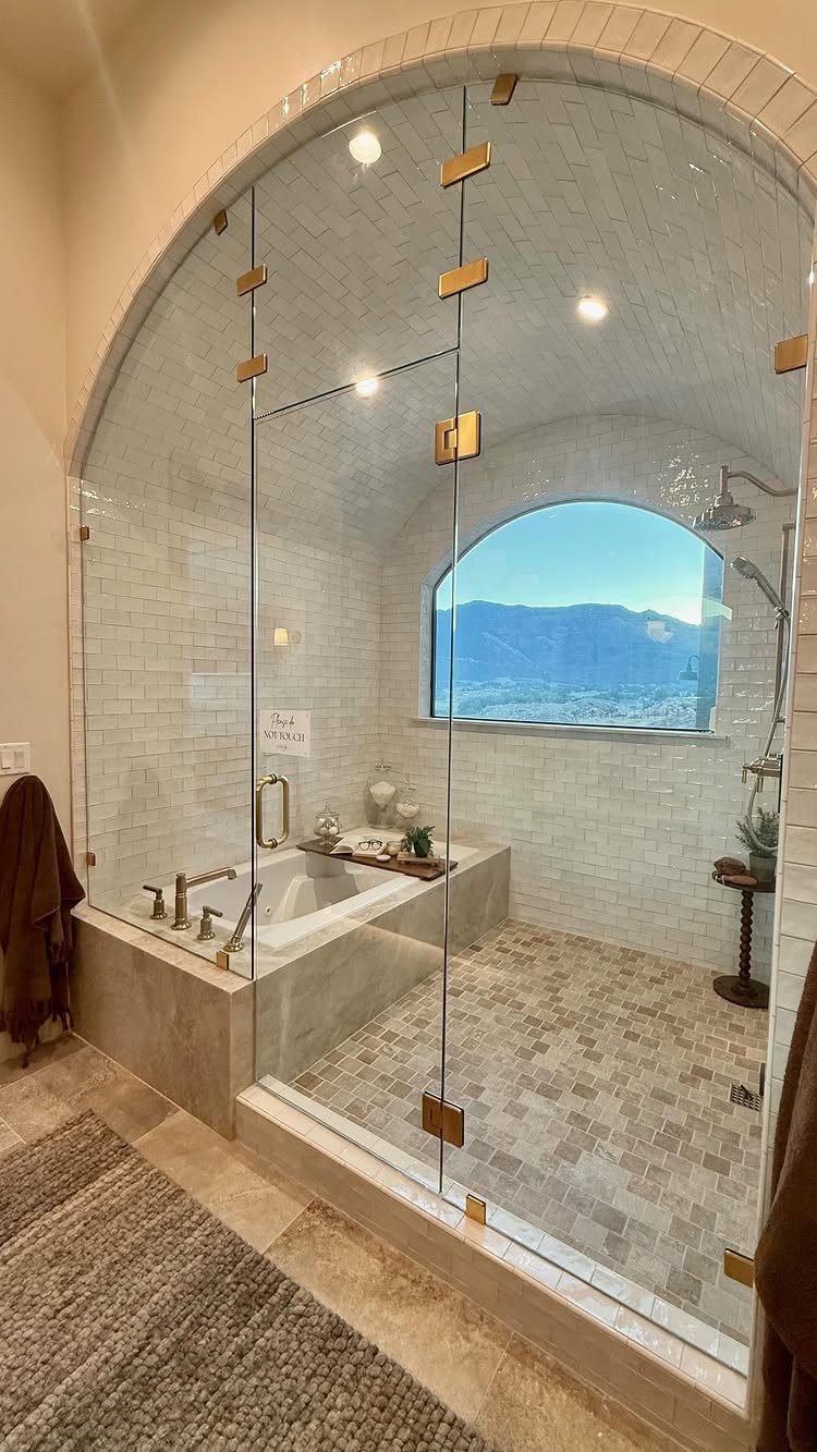 Glass-enclosed bathroom with a built-in bathtub and walk-in shower overlooking mountains.