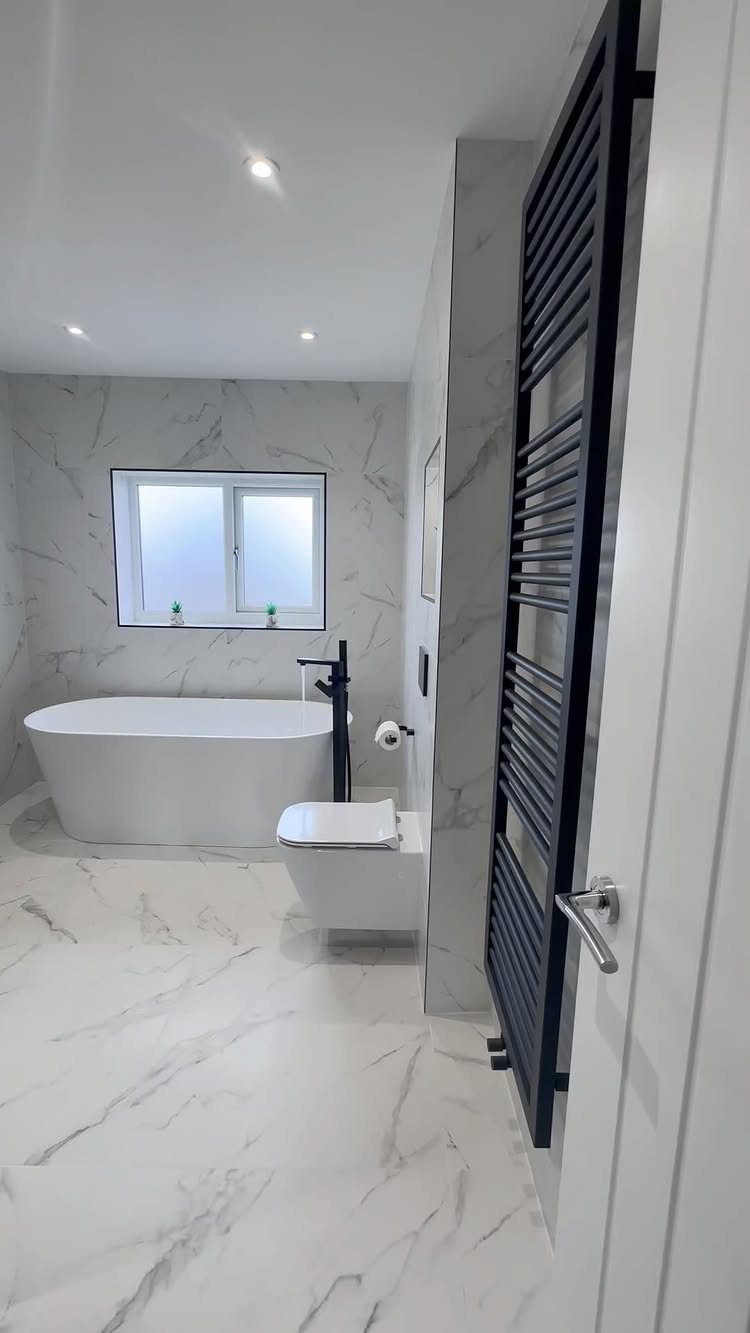 Modern bathroom with white marble surfaces, freestanding tub, and black towel radiator.