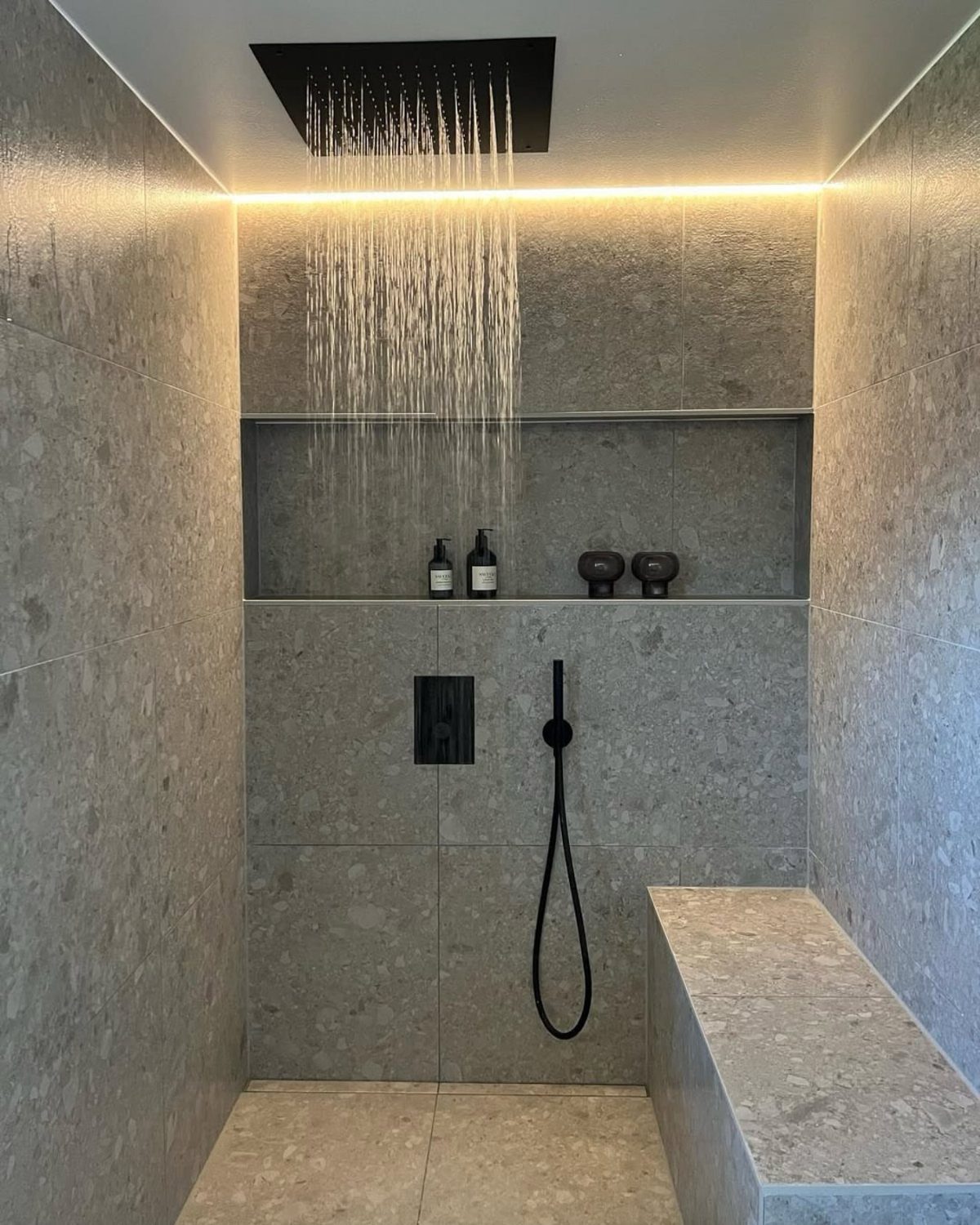 Modern grey stone shower with a rain shower head and recessed wall niche.