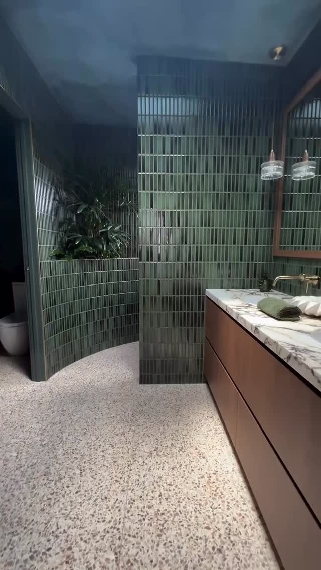 Green vertical kit-kat tiles on a curved bathroom wall with terrazzo flooring.