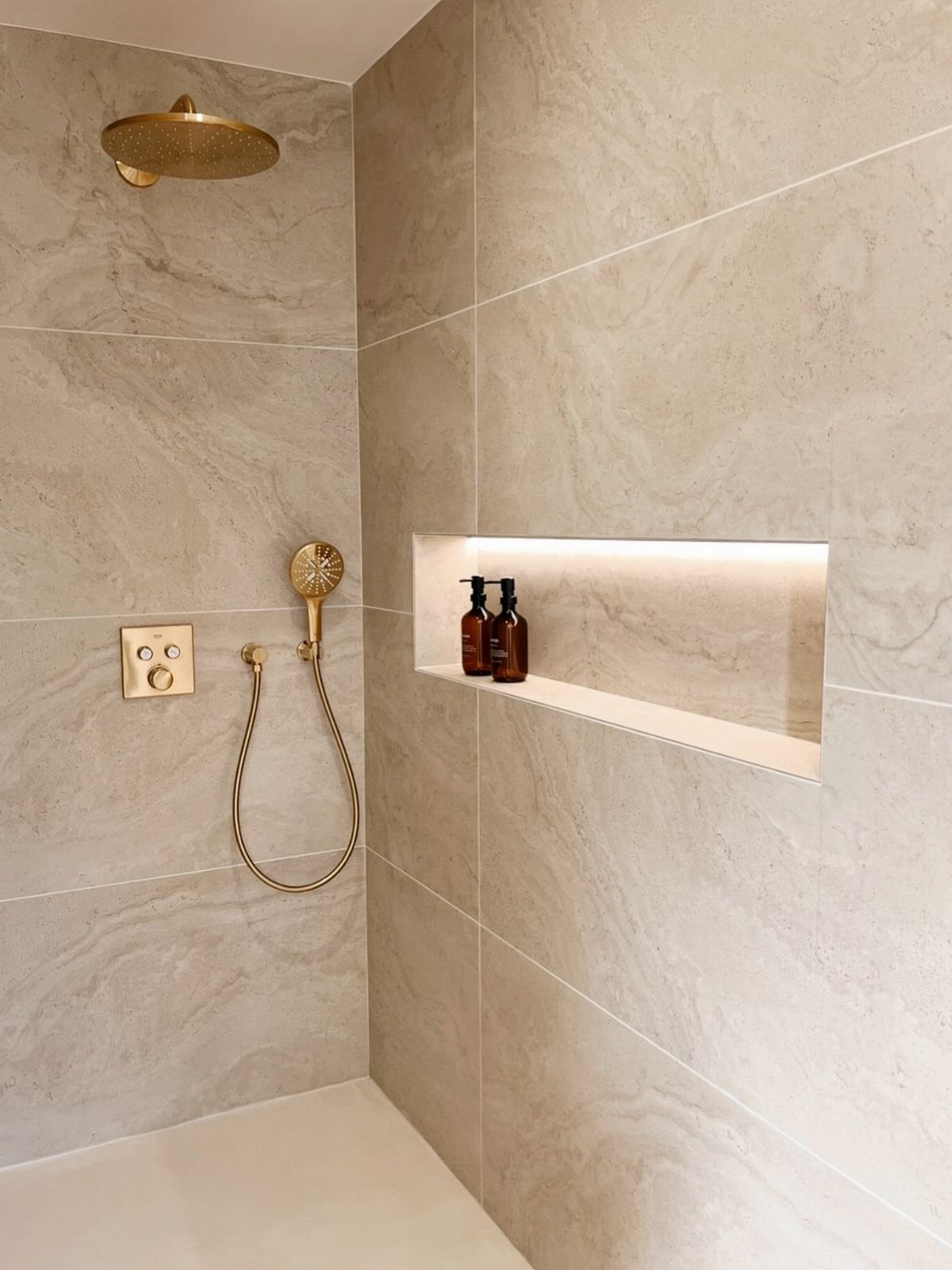 Beige marble-effect shower tiles with gold fixtures and an illuminated recessed wall niche.