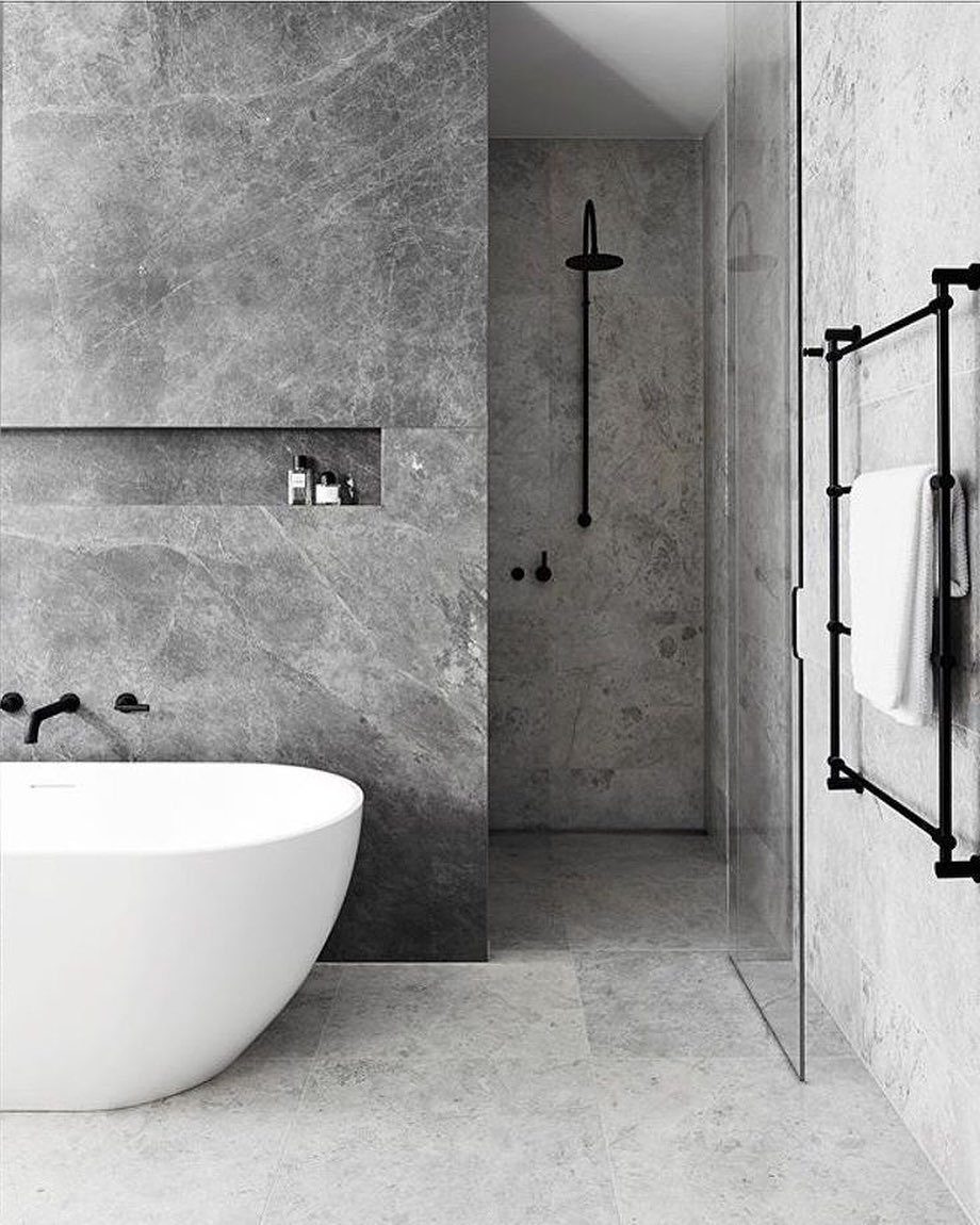 White freestanding bathtub against grey marble-effect wall tiles in a modern bathroom
