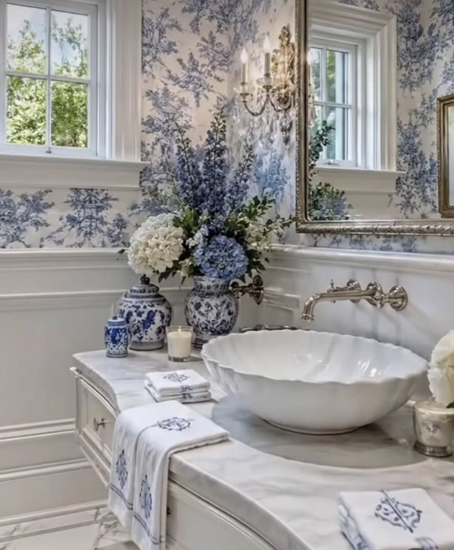 Blue and white floral toile wallpaper in a bathroom with marble countertops and sink.