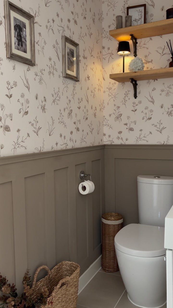 Floral patterned wallpaper and grey wainscoting in a bathroom with a white toilet.