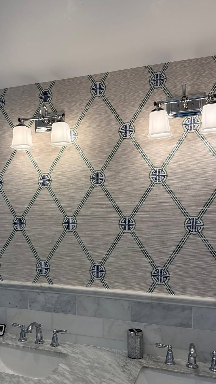 Blue geometric trellis wallpaper in a bathroom with marble counters and chrome lighting.