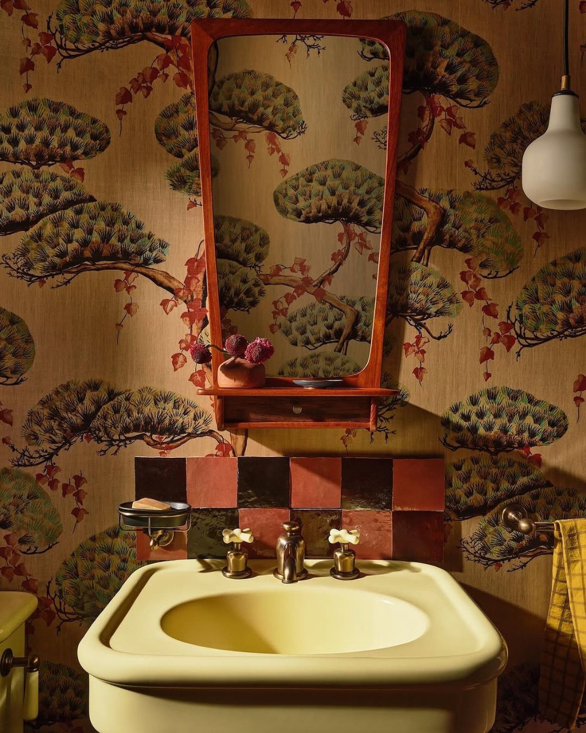 Yellow bathroom sink and red mirror against retro tree pattern wallpaper