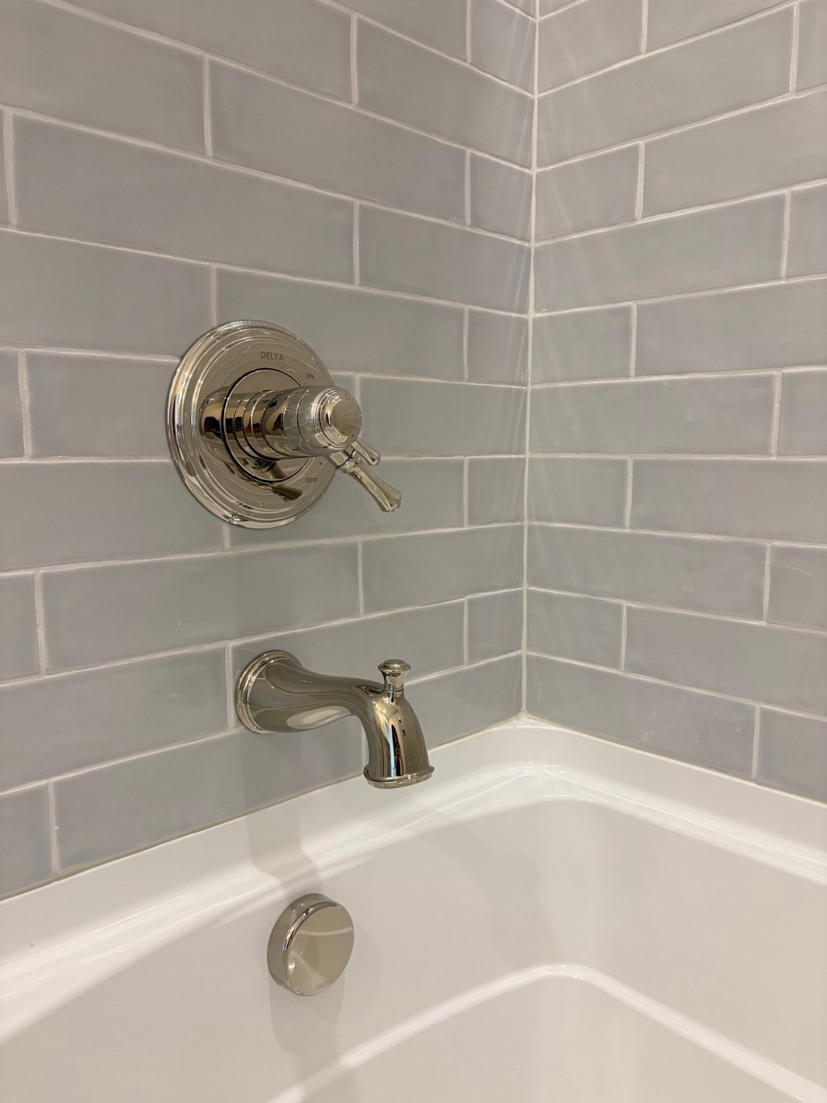 Chrome bathtub faucet and handle installed on grey subway tile walls.