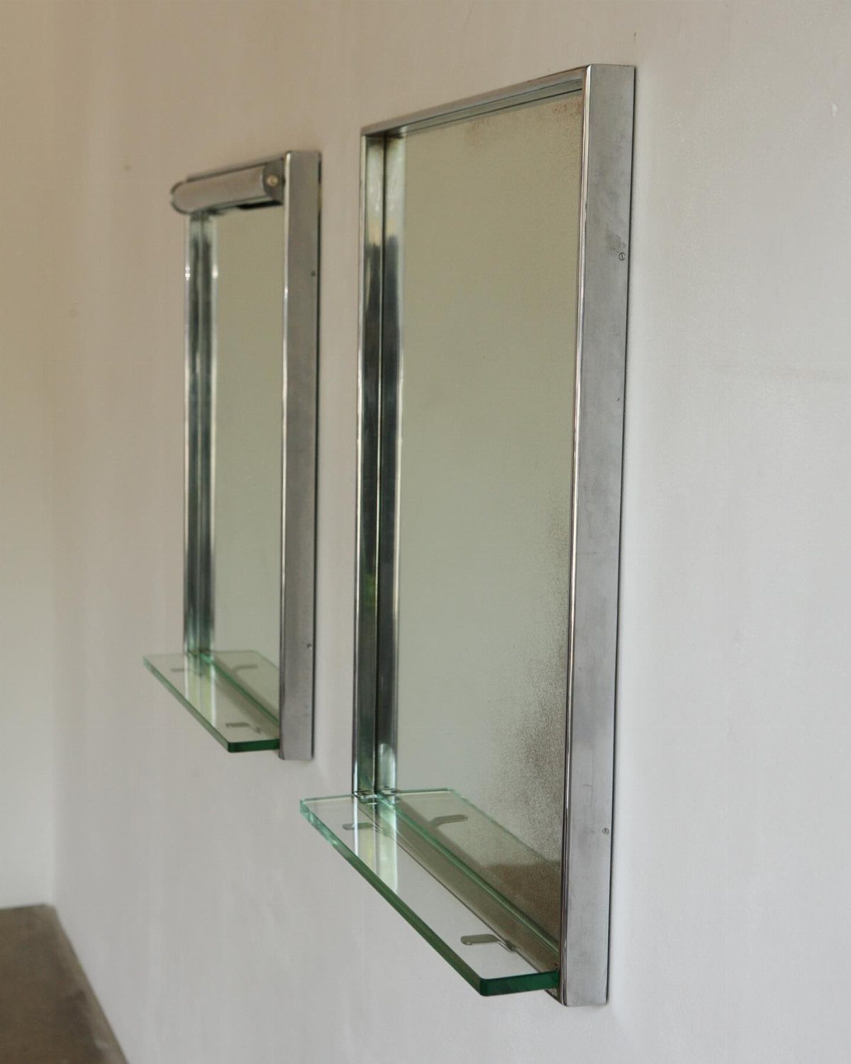 Two chrome framed mirrors with glass shelves mounted on a white wall