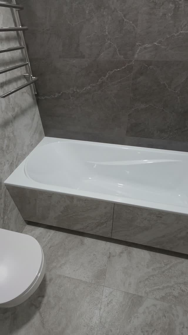 White bathtub and chrome towel rail in a grey marble tiled bathroom
