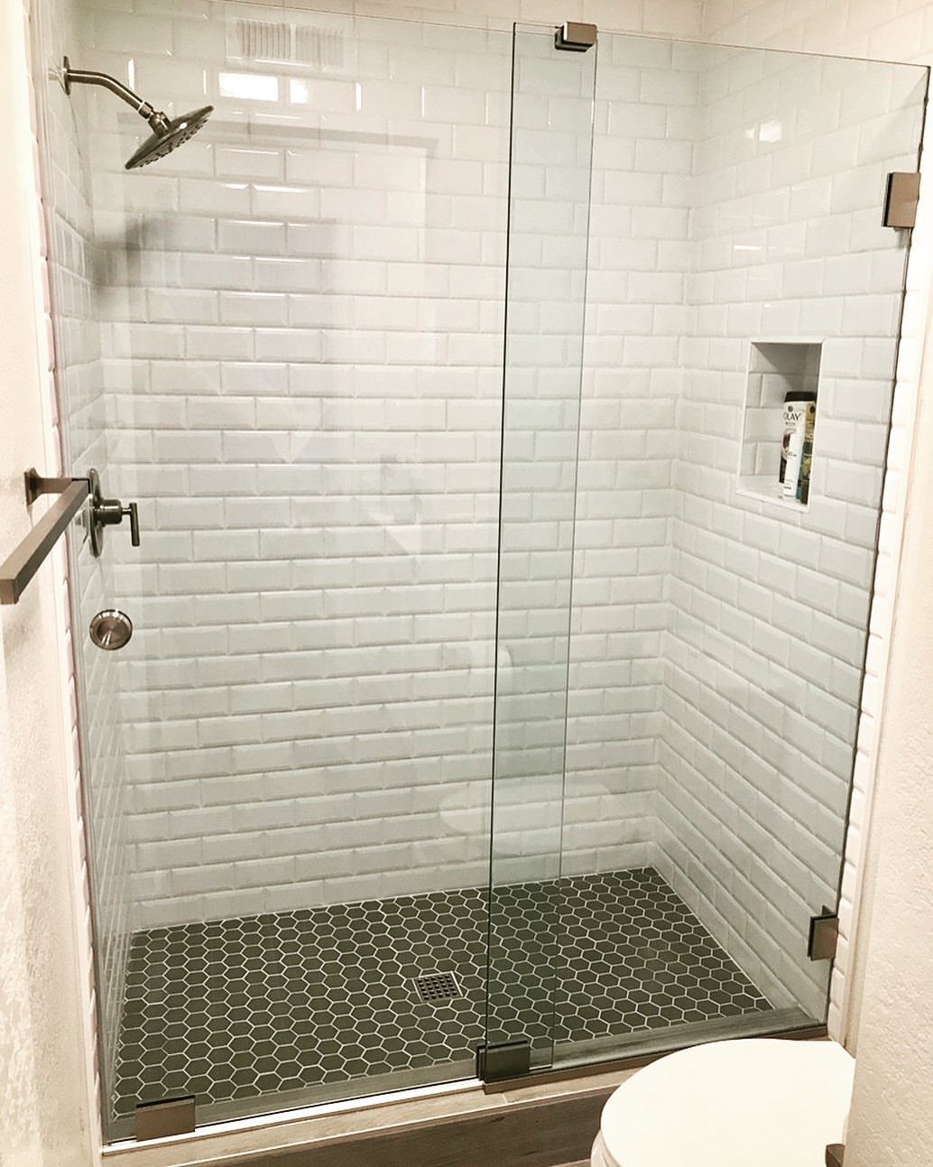 Glass shower doors with white subway tiles and dark hexagonal floor tiles.