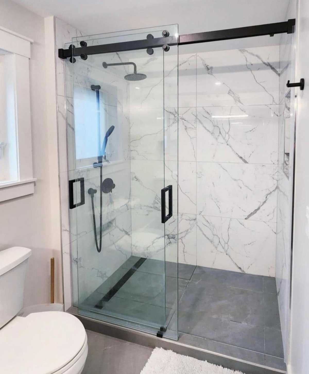 Clear glass sliding shower doors with black hardware and white marble walls.