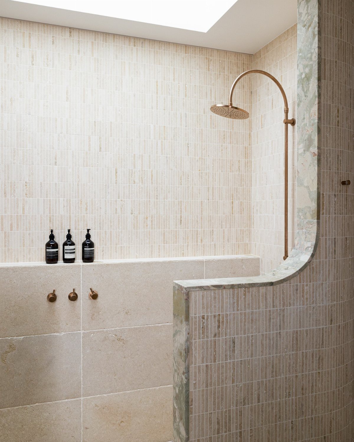 Modern shower with beige vertical tiles, a built-in bench, and gold fixtures.