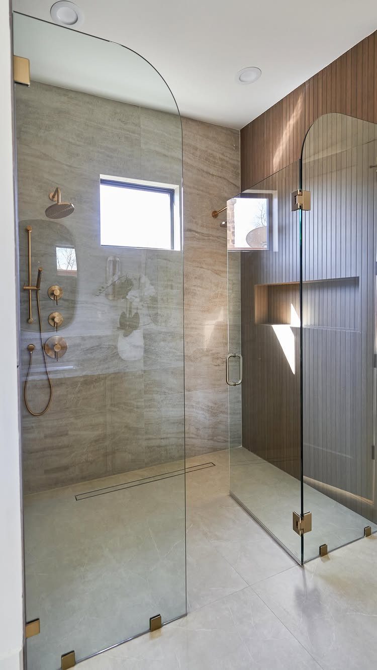 Curved glass shower enclosure with gold hardware and grey stone tile walls.