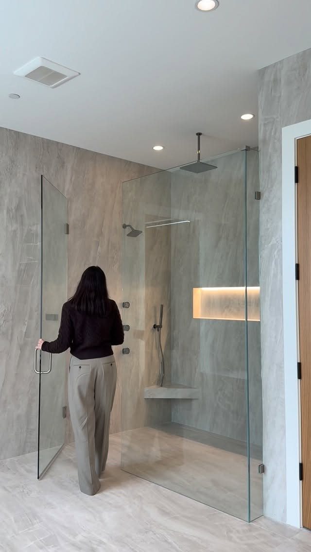 Frameless glass shower enclosure with grey marble tiles and a built-in bench.