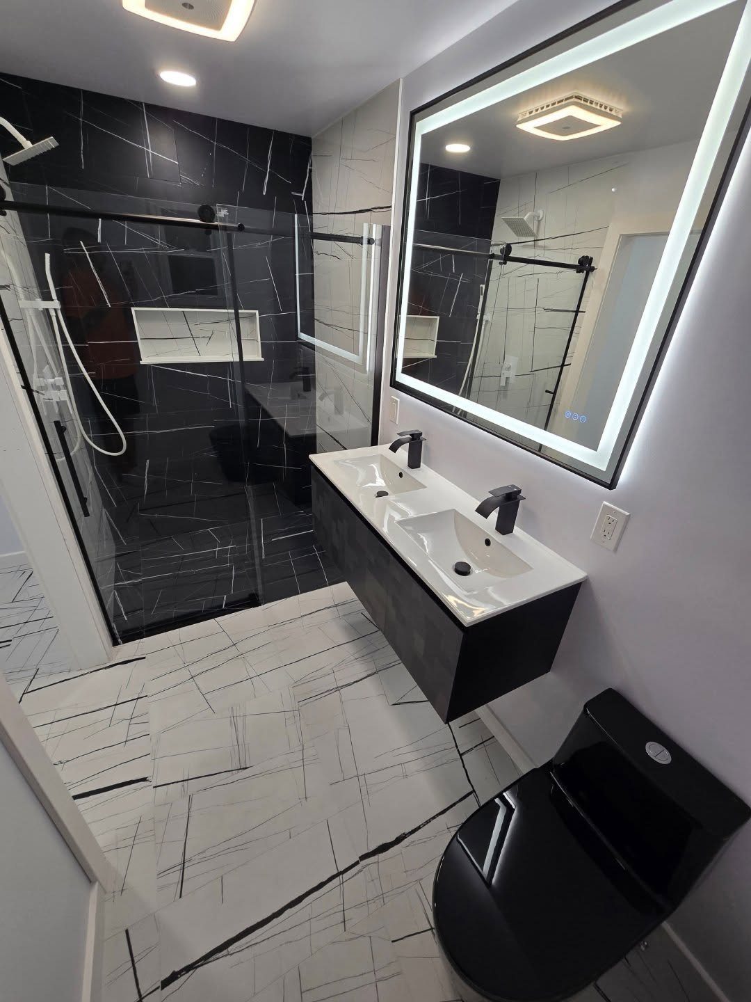 Modern bathroom with glossy black shower tiles, black vanity, and white marble floors.