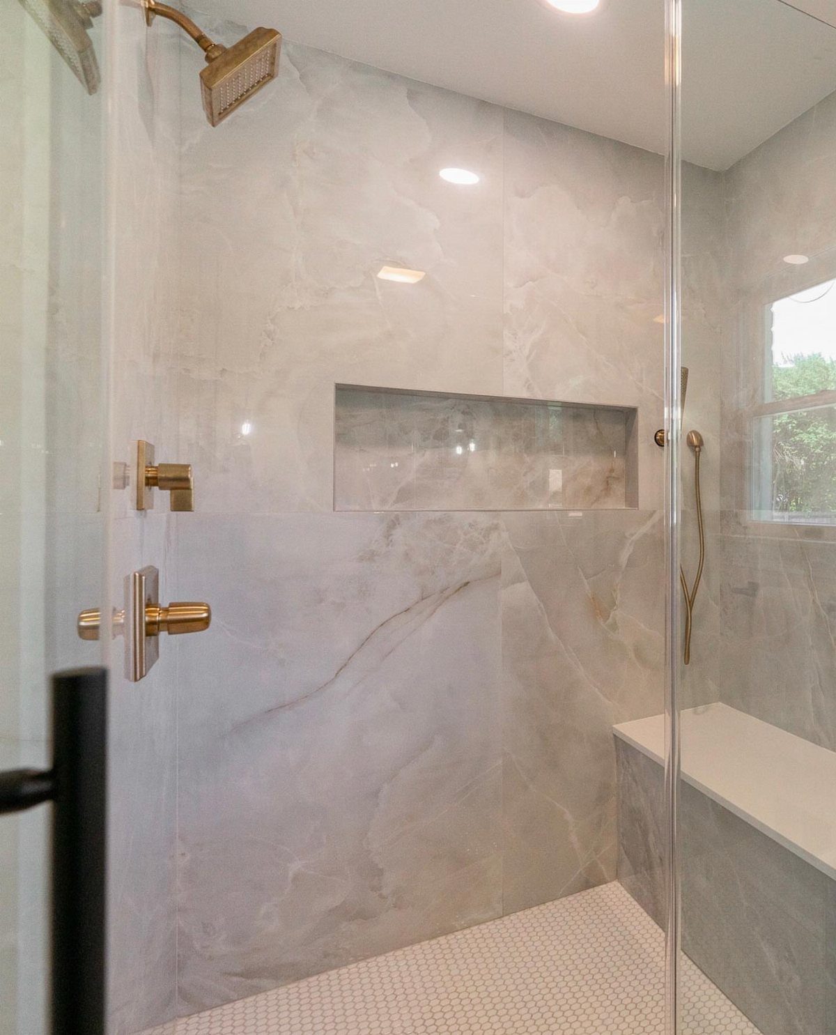 Modern walk-in shower with large-format marble tiles and gold fixtures.