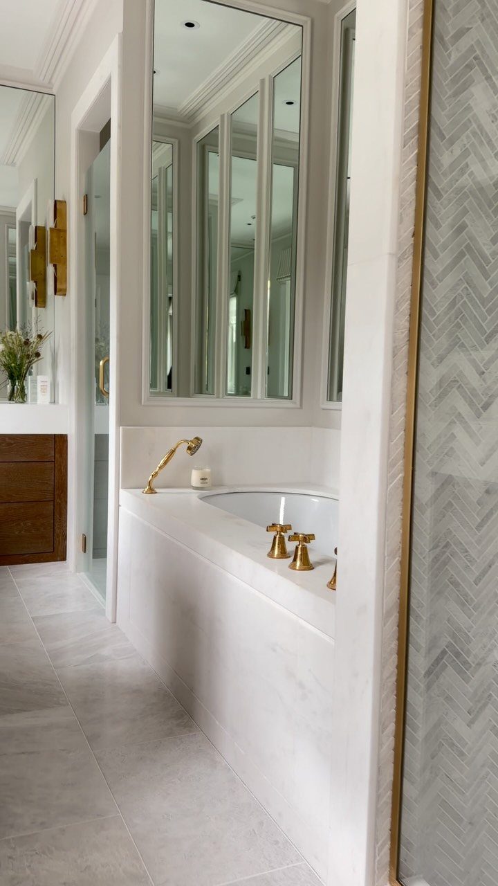 White marble bathtub with gold fixtures and light grey marble floor tiles.