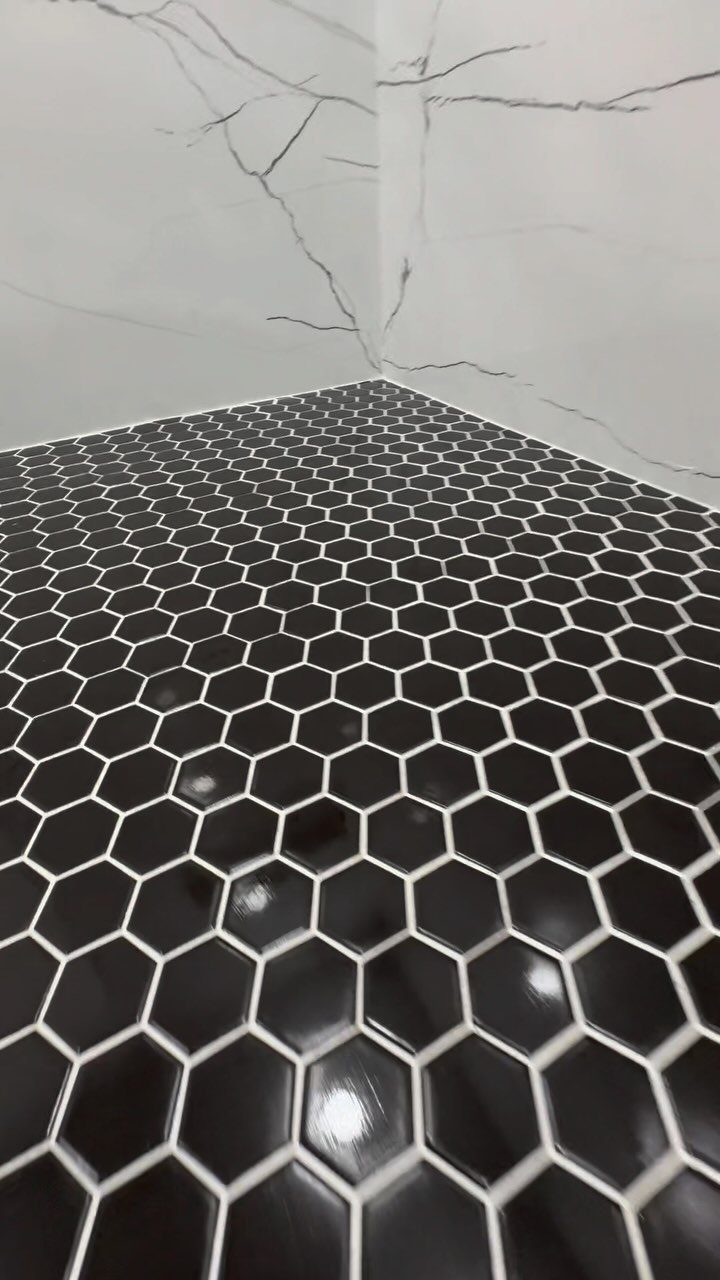 Black hexagonal floor tiles meeting white marble walls in a modern shower