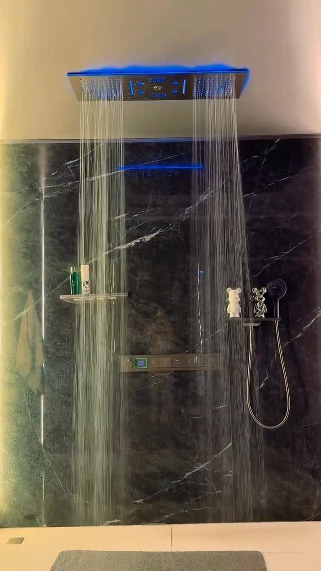 Ceiling-mounted rainfall showerhead with blue lighting against dark marble bathroom walls.
