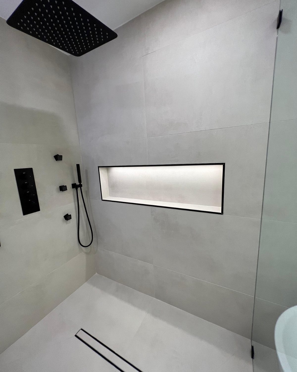 Modern white shower featuring a long, illuminated rectangular recessed wall niche for storage.