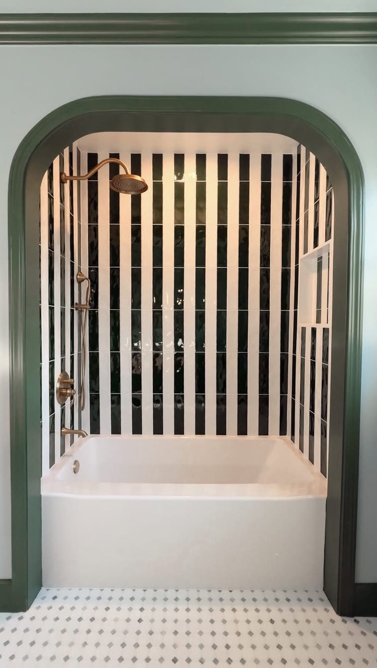 White bathtub with vertical black and white striped tile walls in an arched alcove
