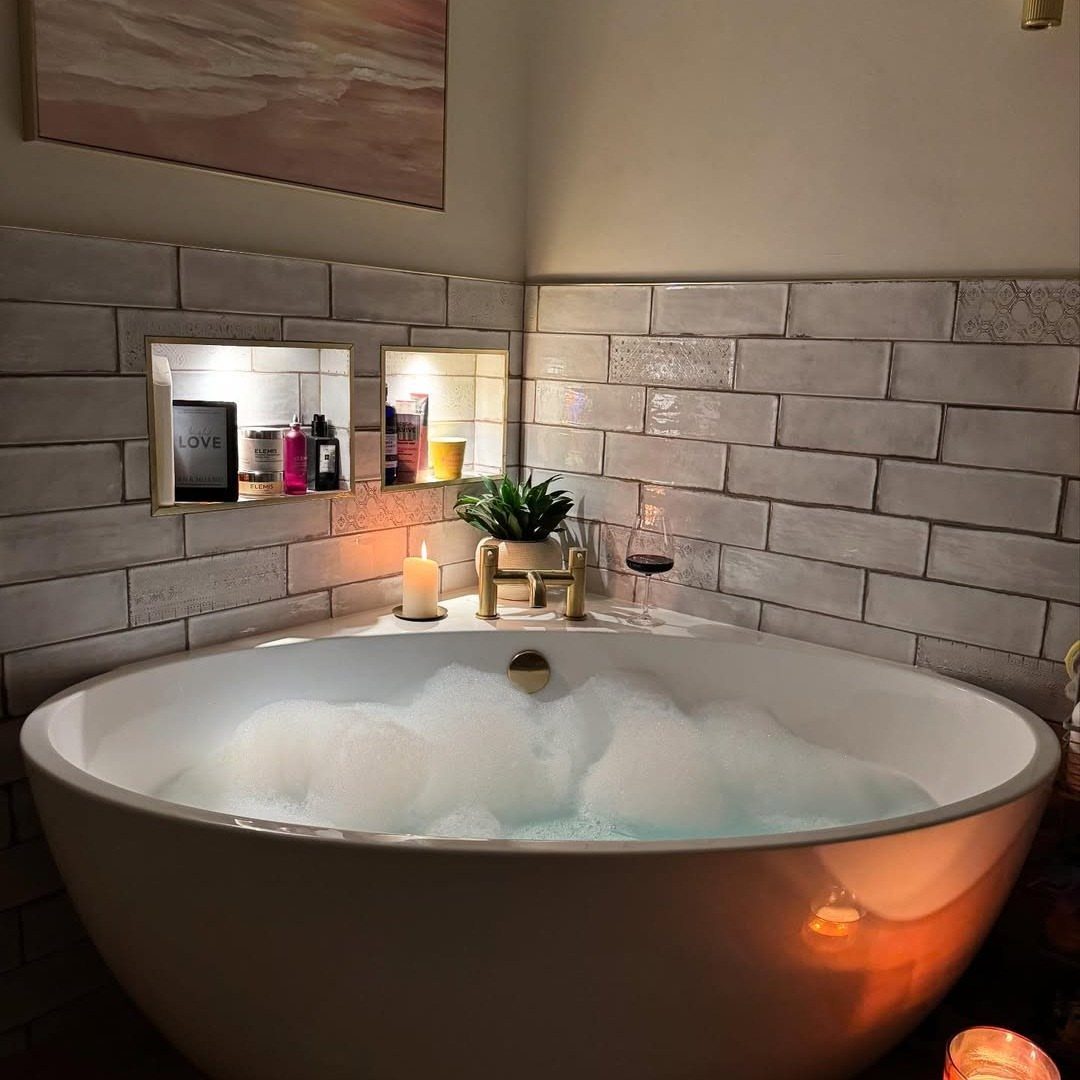 White bubble bath in a corner with grey tiled walls and gold fixtures