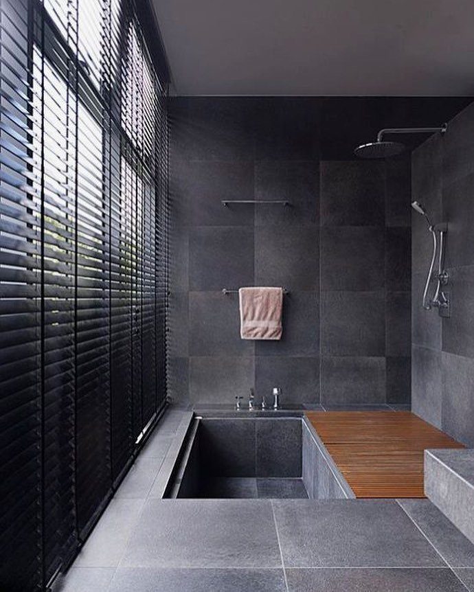 Sunken rectangular bathtub surrounded by dark grey tile walls and a wooden deck.