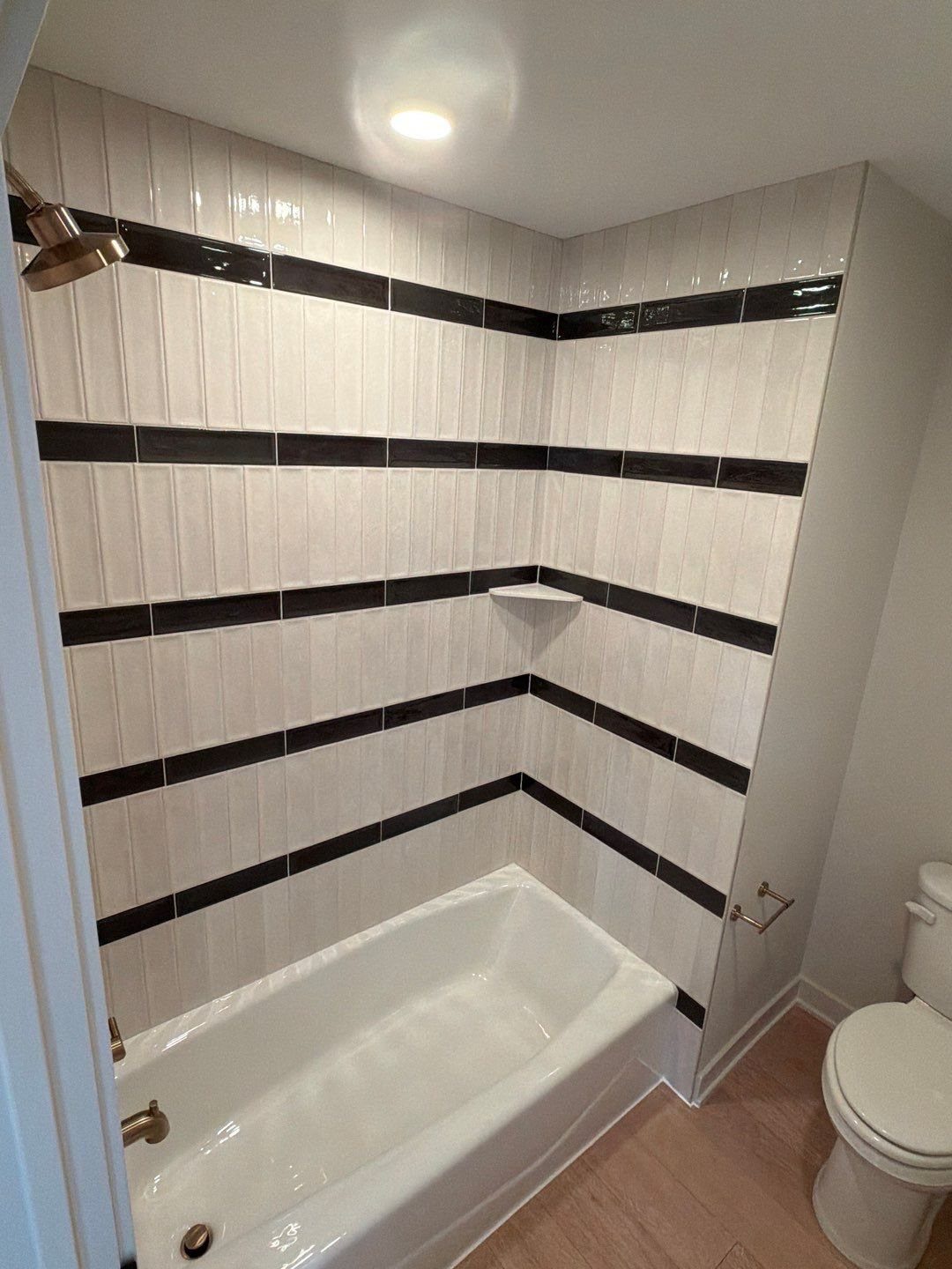 White bathtub with white tiled walls featuring horizontal black accent stripes