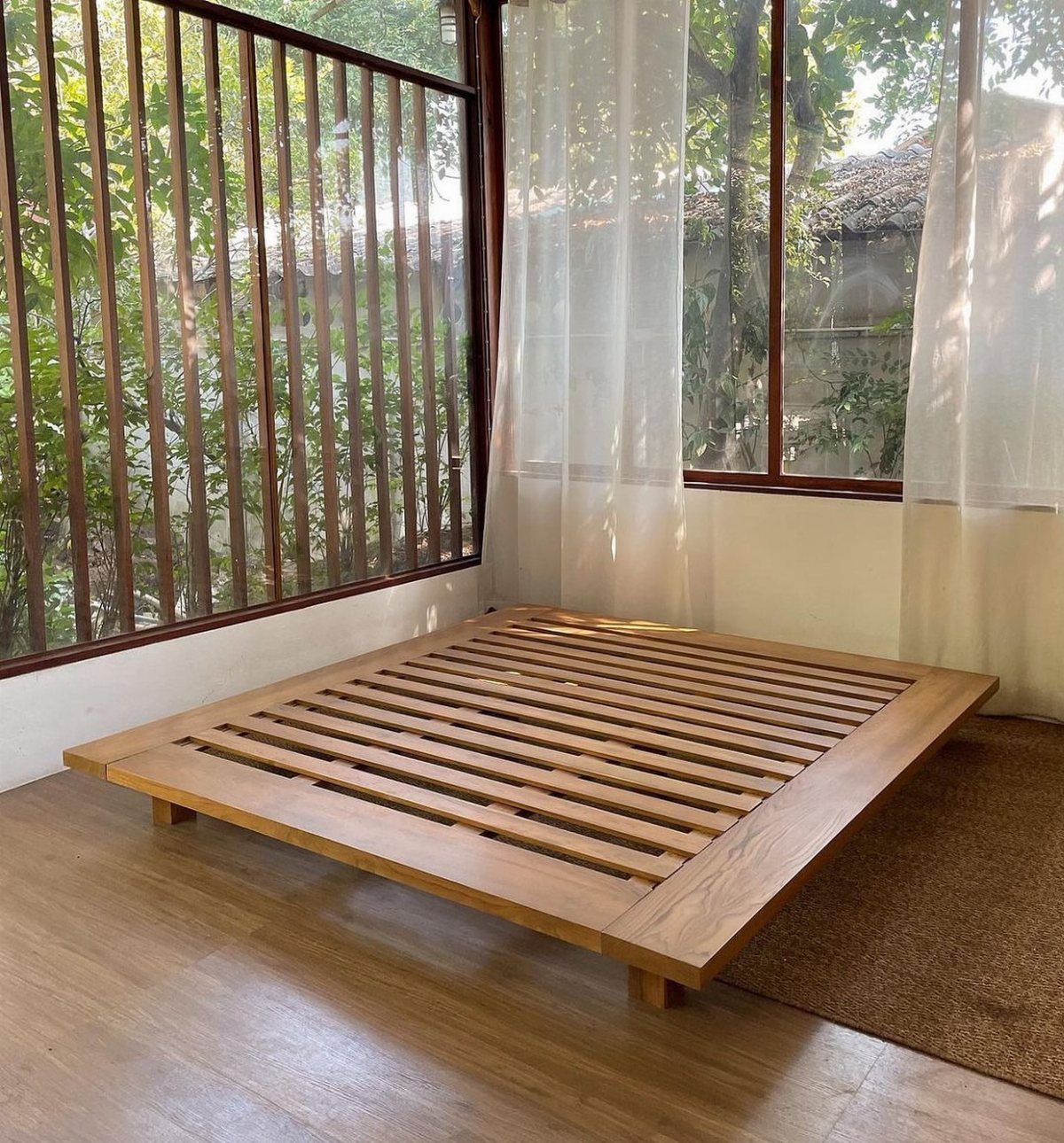 Wooden platform bed frame with exposed legs and slatted base in bright room