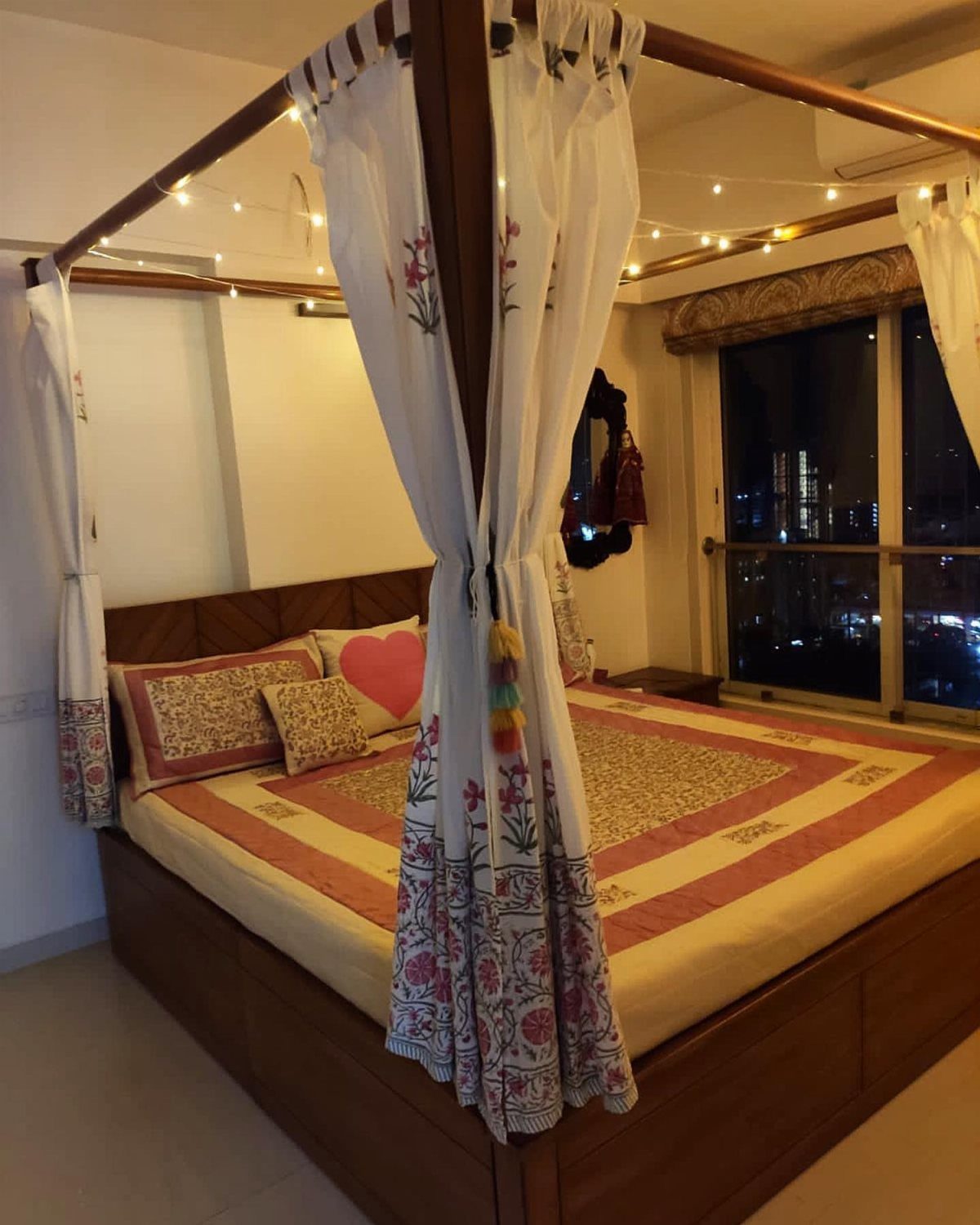 Four-poster bed with white floral curtains and string lights in a bedroom