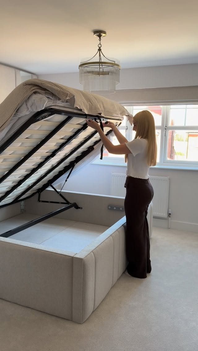 Woman lifting a storage bed mattress in a bright, minimalist white bedroom.