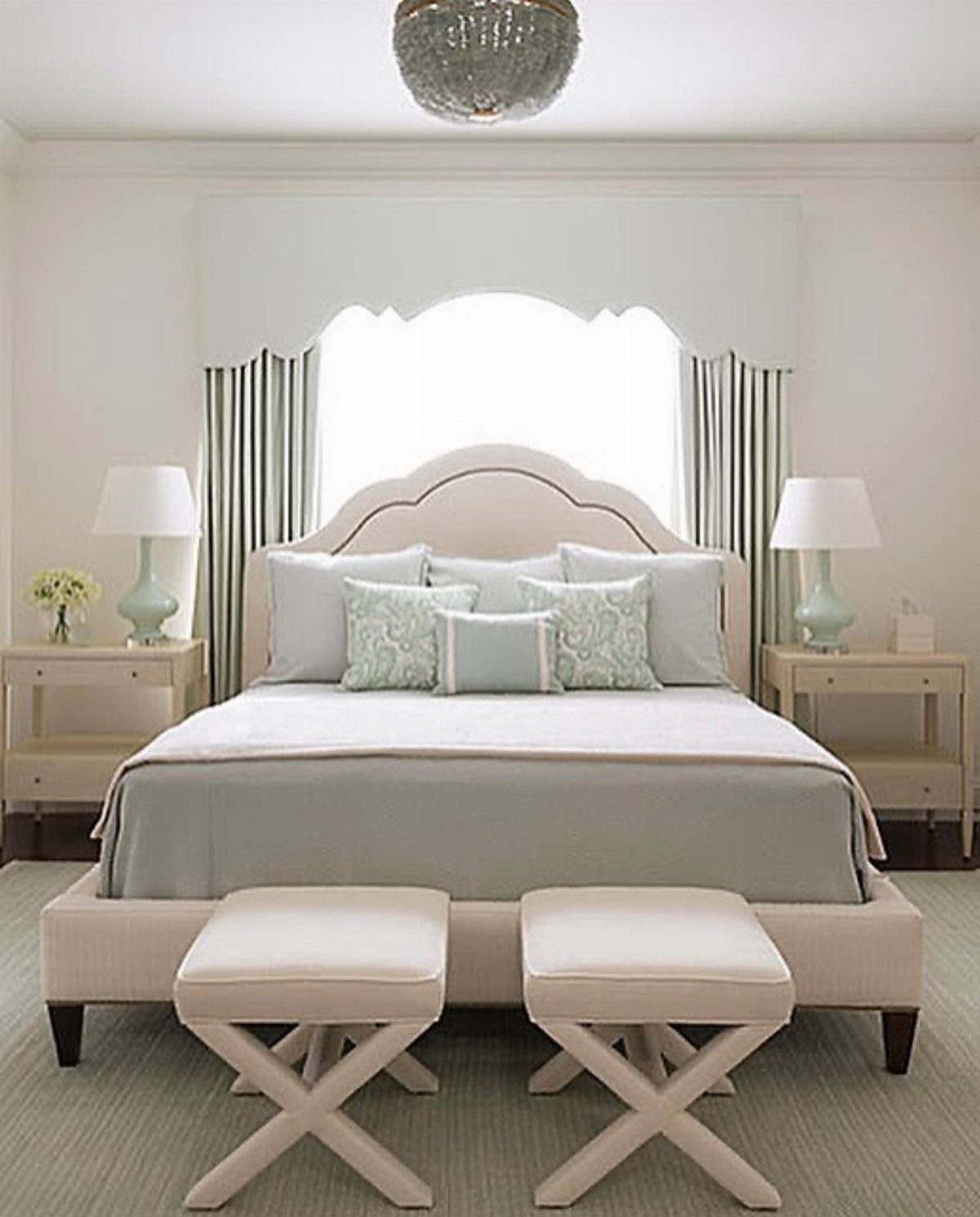 Large bed with light blue linens positioned in front of a bright window.