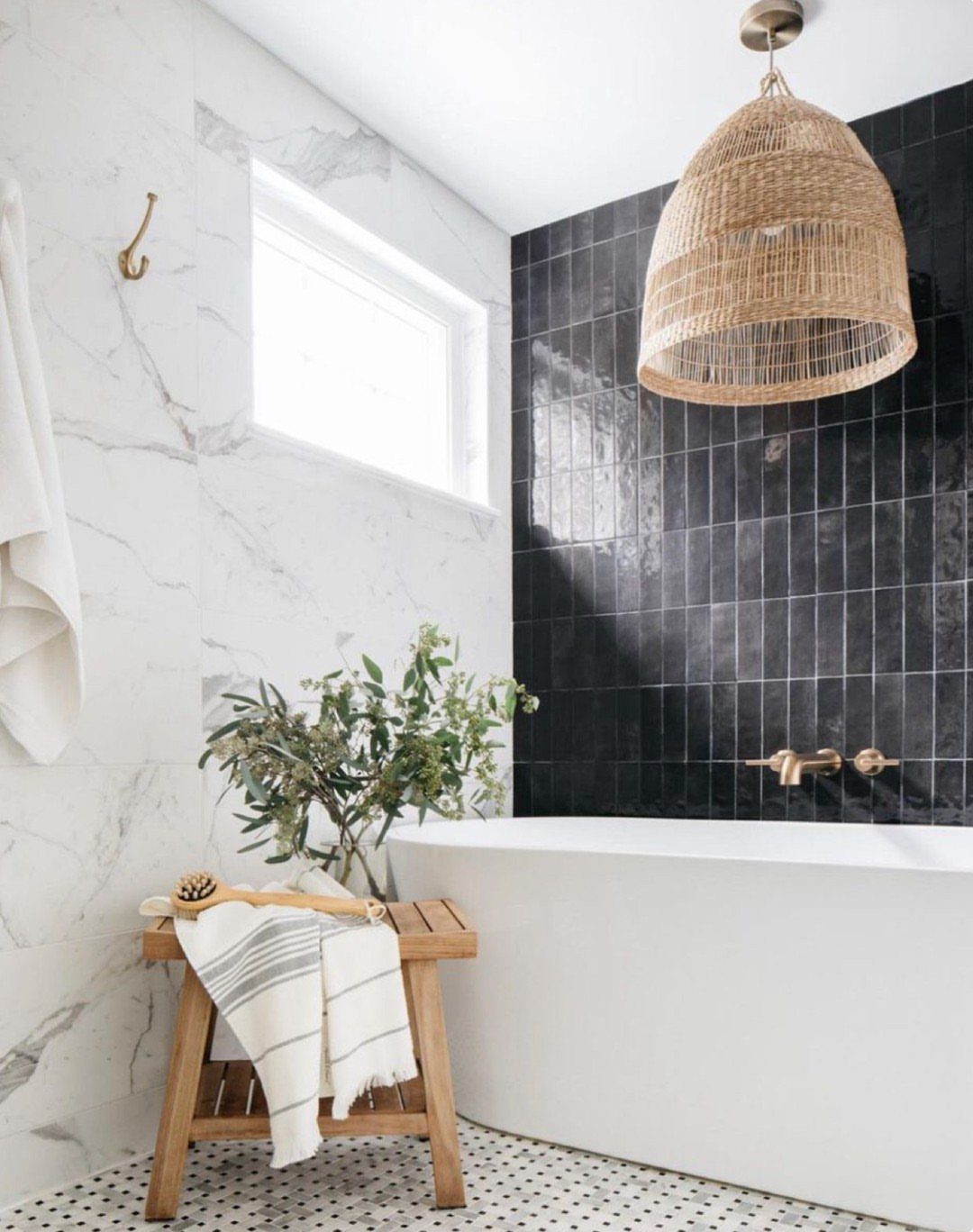 White freestanding bathtub against black tiled wall with white marble walls and mosaic flooring.