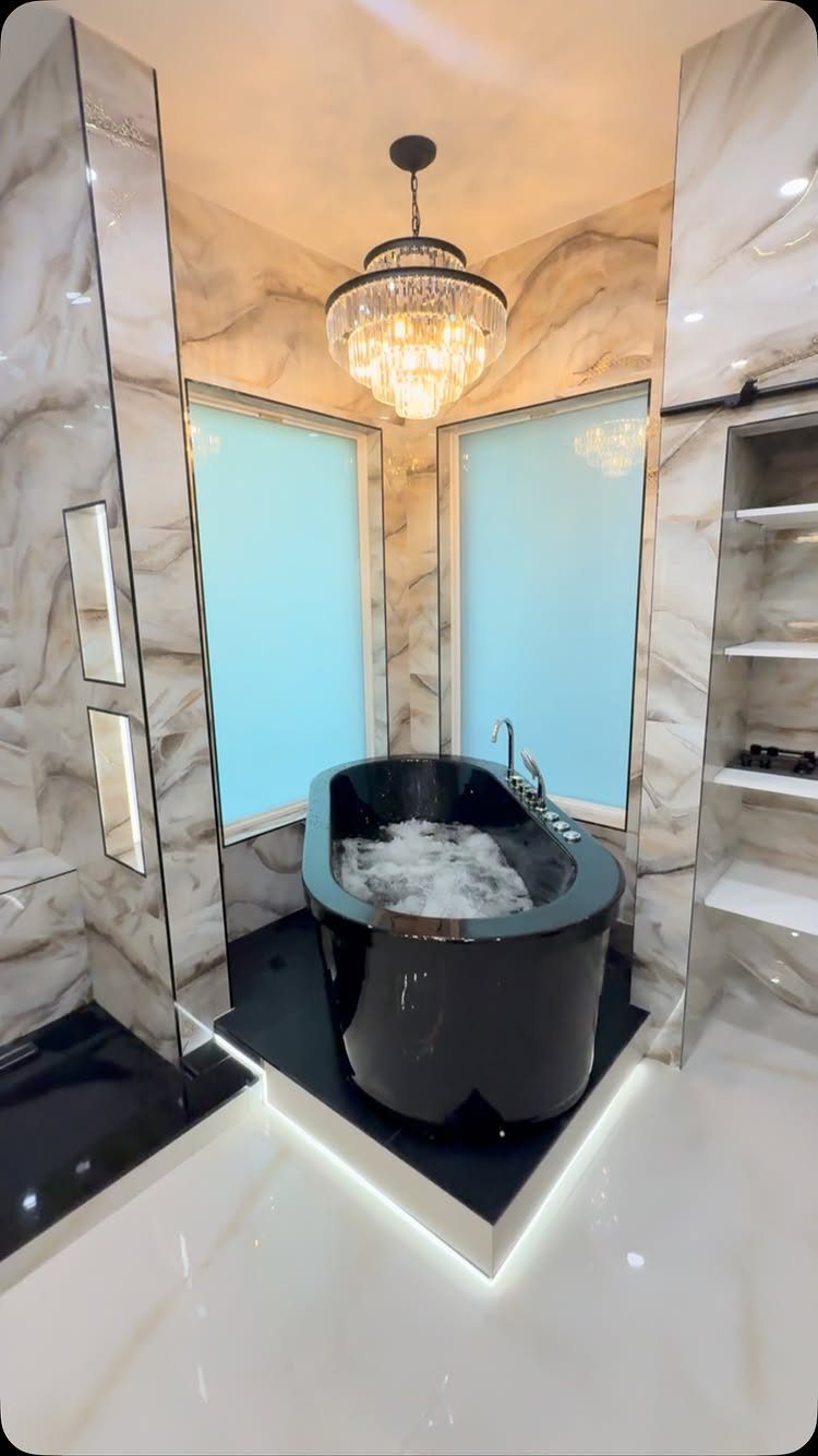 Black freestanding bathtub in a white marble bathroom with a crystal chandelier.