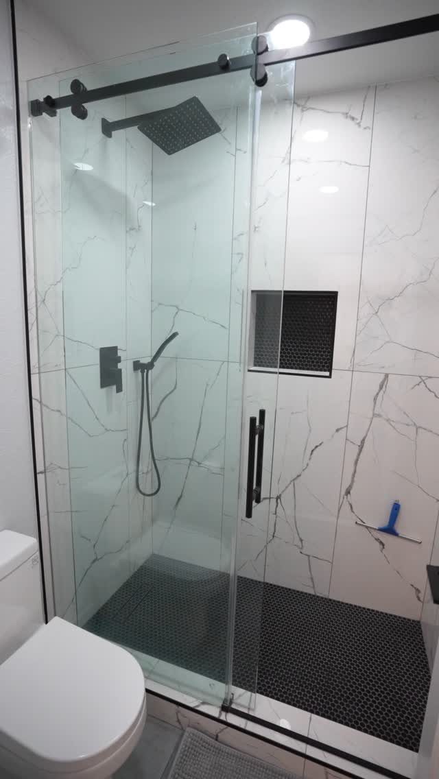 White marble bathroom walls with a black tiled shower floor and glass door.