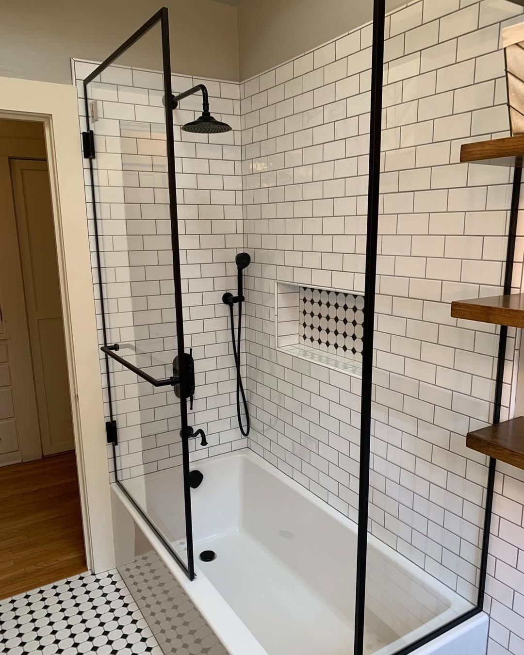 White tiled bathroom with black shower frame, built-in tub, and patterned floor tiles.