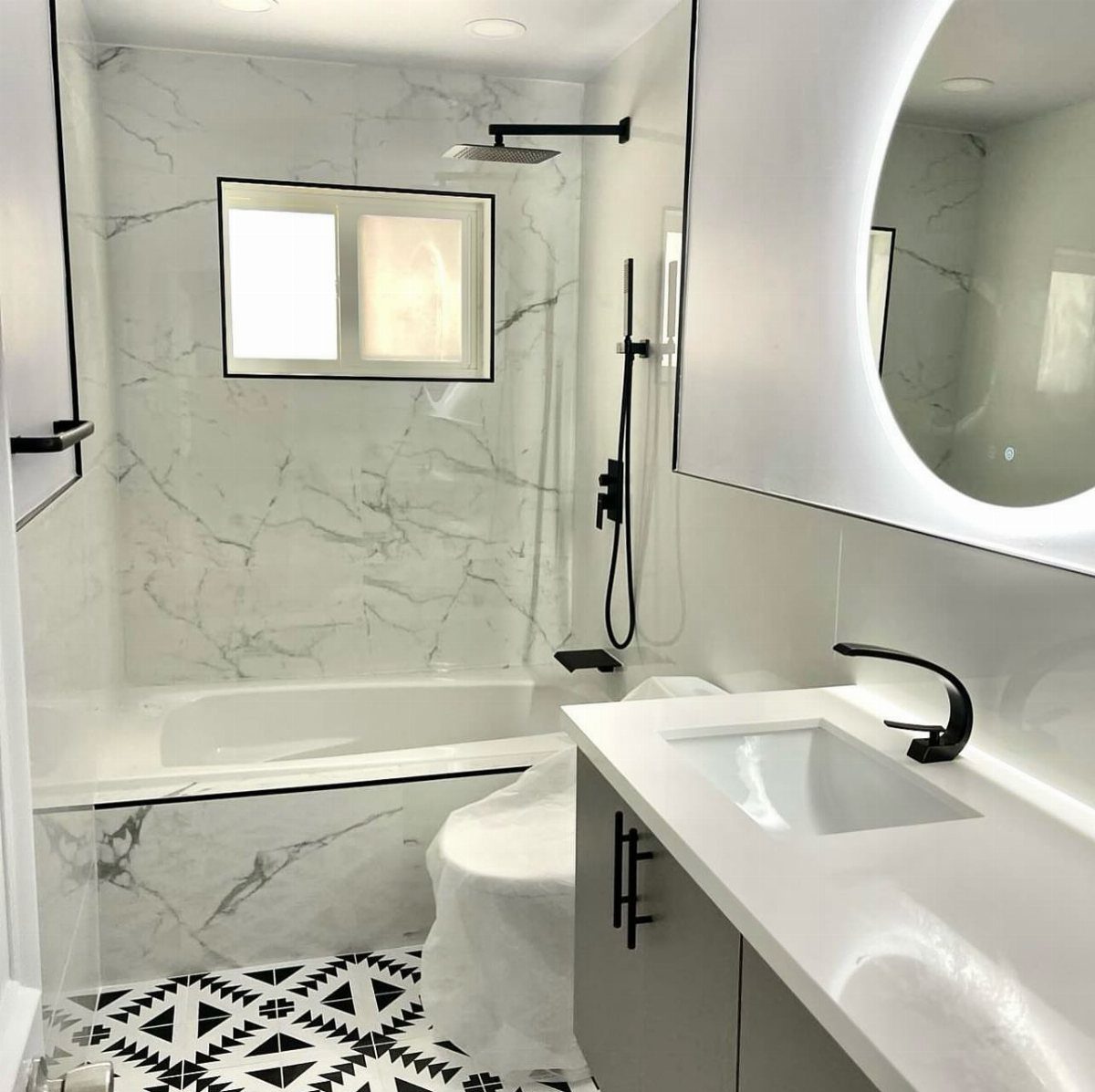 Modern bathroom with white marble walls, white tub, and geometric black and white tiles.