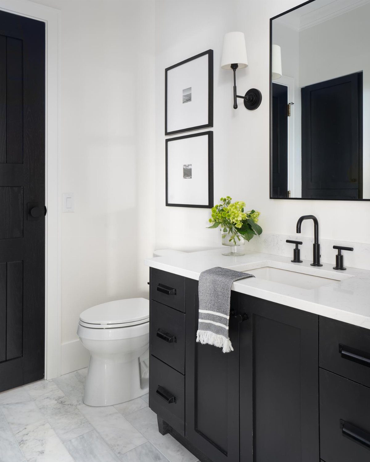 Black vanity and white walls in a monochrome powder room with marble floors.
