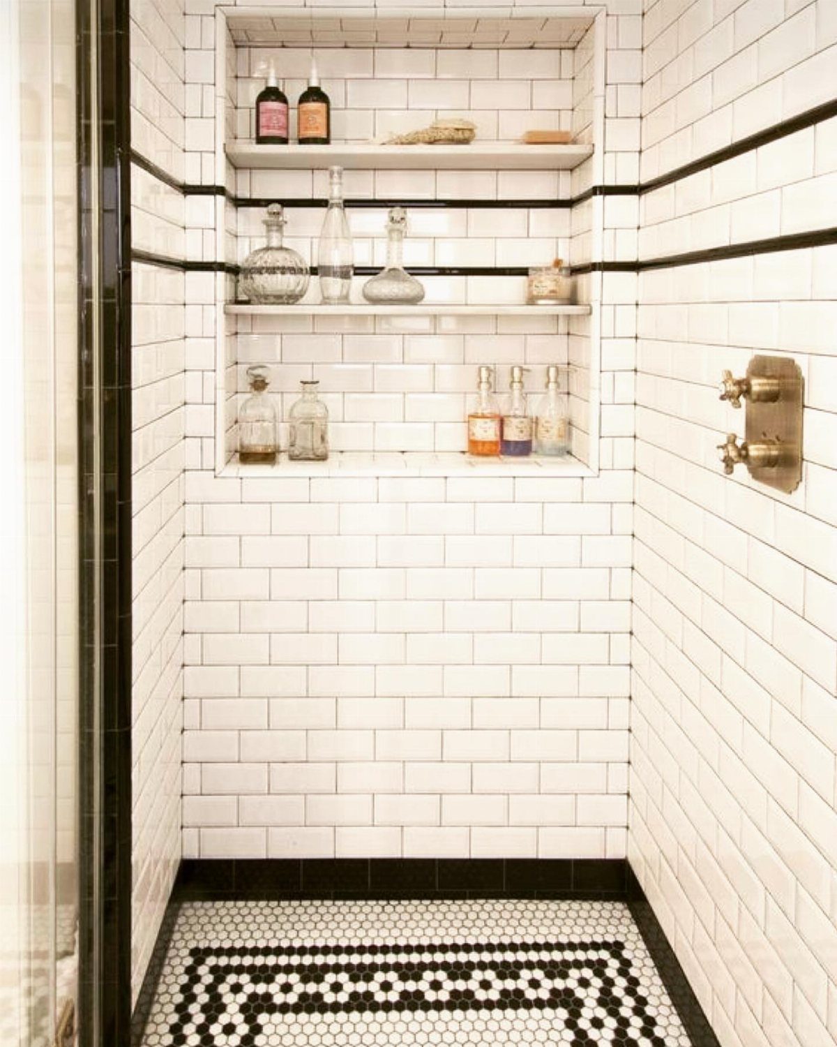 White subway tile shower with black accents and patterned penny tile floor